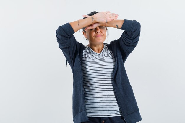 Donkerharige vrouw met haar omgekeerde handen op haar voorhoofd in shirt