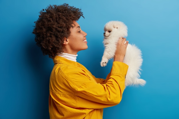 Gratis foto donkerhuidige dame houdt lippen rond, wil schattig huisdier kussen, speelt met kleine puppy