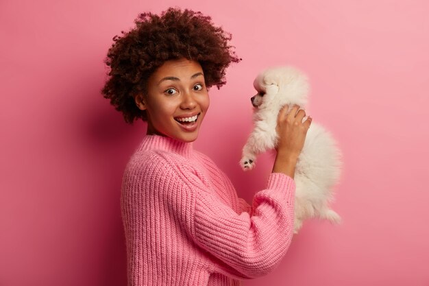 donkerhuidige dame houdt lippen rond, wil schattig huisdier kussen, speelt met kleine puppy