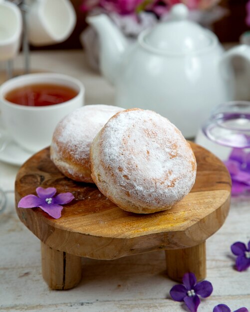 Donuts gegarneerd met bloemsuiker en een kopje zwarte thee