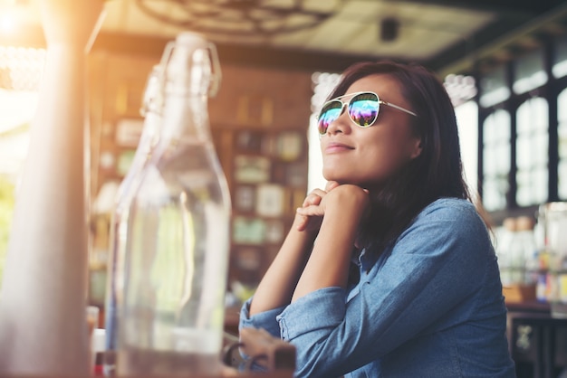 Doordachte jonge hipster vrouw met een bril zitten aan tafel bij