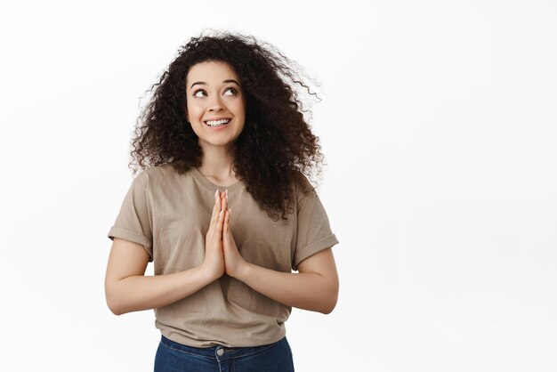 Doordachte jonge vrouw die aan iets leuks torenvingers denkt terwijl ze nadenkt, maakt een plan om te beslissen wat ze moet doen en glimlacht terwijl ze naar de rechterbovenhoek witte achtergrond kijkt