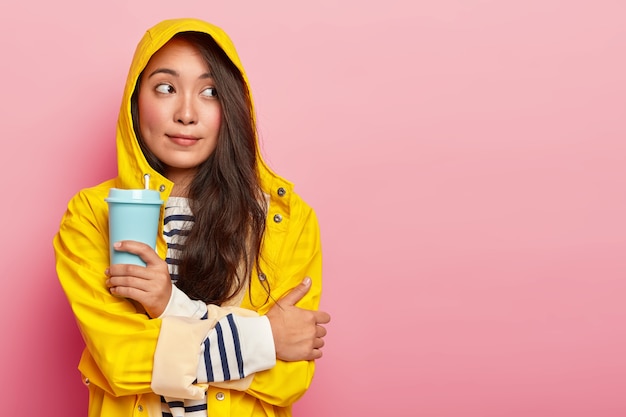 Doordachte jonge vrouw van gemengd ras voelt het koud, drinkt warme drank om zichzelf op te warmen, beeft na het lopen tijdens zware regenval