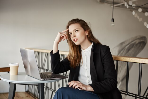 Doordachte jonge vrouwelijke freelancer werken in café met laptop, denken