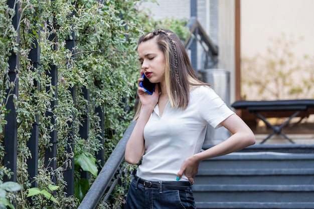 Doordachte jongedame die bij de trap staat en aan de telefoon praat