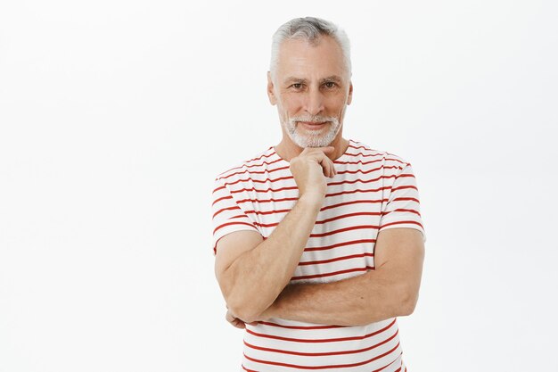 Doordachte lachende senior man in t-shirt op zoek met tevreden uitdrukking