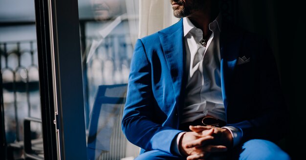 Doordachte man in blauwe pak zit op de vensterbank