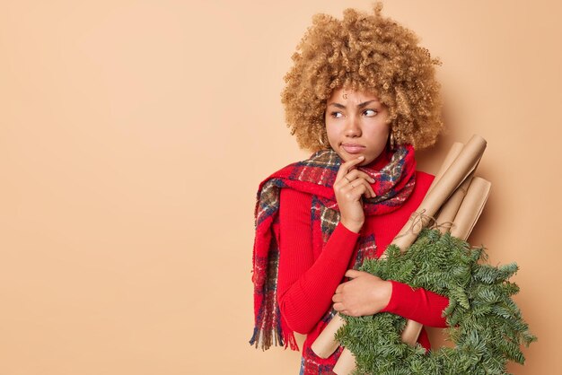 Doordachte serieuze vrouw geconcentreerd weg betrokken bij ambacht draagt items voor decoratie voor wintervakanties draagt warme winter sjaal om nek geïsoleerd over beige achtergrond lege ruimte