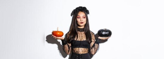Doordachte stijlvolle vrouw in heksenkostuum die pompoen plukt voor halloween die een beslissing neemt terwijl ze standi