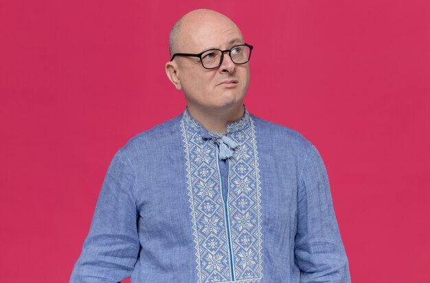 Doordachte volwassen Slavische man in blauw shirt met optische bril die omhoog kijkt