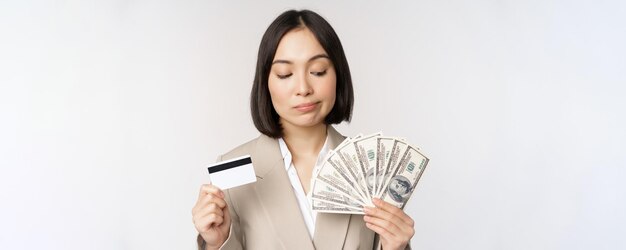 Doordachte zakenvrouw Koreaanse zakelijke vrouw die creditcard en geld contante dollars in handen toont die zich over witte achtergrond bevinden en denken