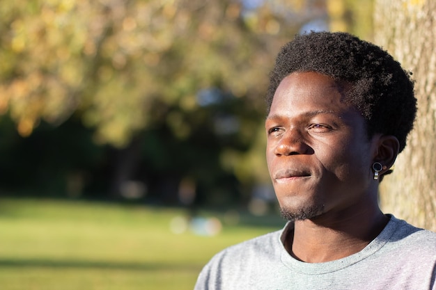 Doordachte zwarte man die tijd buiten doorbrengt in het stadspark. Portret van een knappe Afro-Amerikaanse man in een grijs T-shirt die opzij kijkt en denkt. Close-up shot. Jeugd, levensstijl, vrije tijd concept.