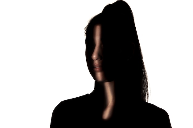 Dramatisch portret van een jong meisje in het donker dat op witte studiomuur wordt geïsoleerd