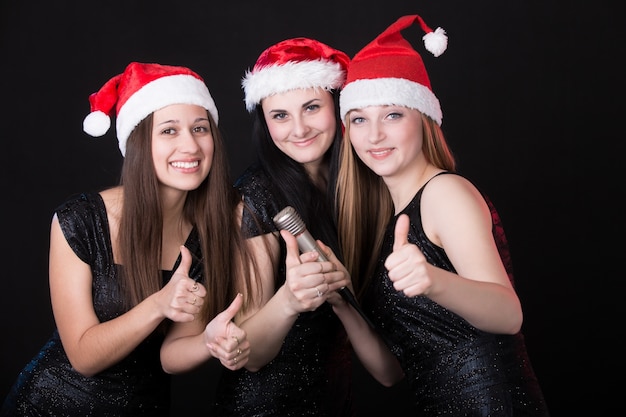 Drie aantrekkelijke santa meisjes met een microfoon die 