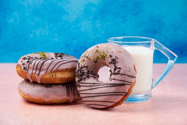 Drie aardbeidonuts met een glas melk op roze lijst.