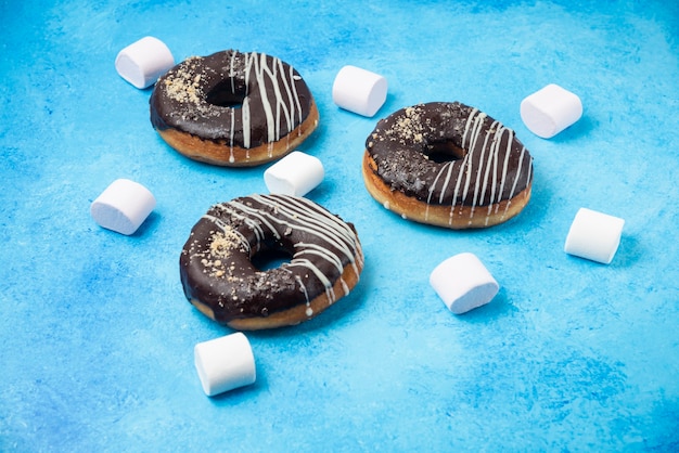 Drie chocolade donuts en marshmallows op blauwe ondergrond.