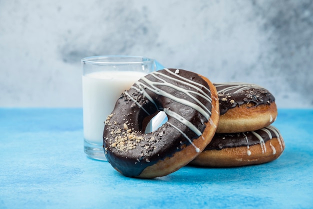 Drie chocolade donuts met een glas melk op blauwe tafel.