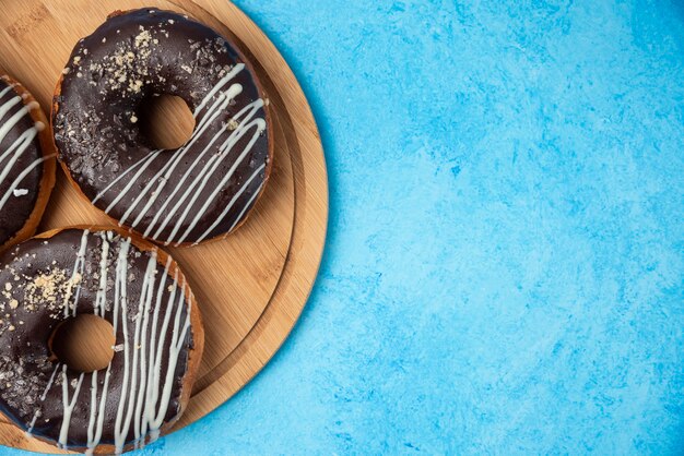 Drie chocolade donuts op houten plaat en op blauwe achtergrond.