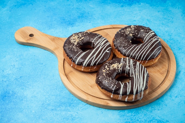 Drie chocolade donuts op houten plaat en op blauwe ondergrond.