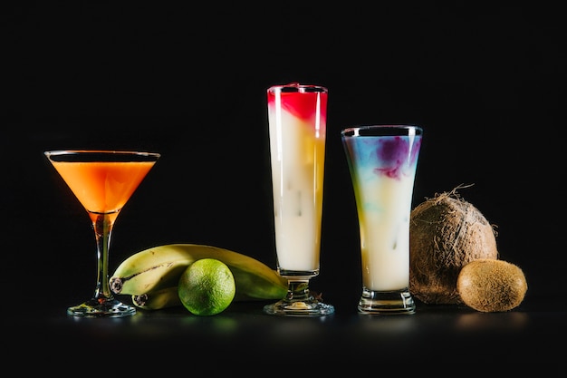 Drie cocktails en exotisch fruit op zwarte achtergrond