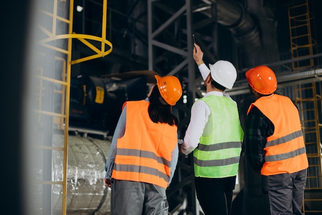 Drie fabrieksarbeiders met veiligheidshoeden bespreken fabricageplan