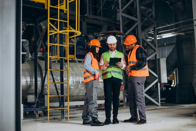 Drie fabrieksarbeiders met veiligheidshoeden bespreken fabricageplan