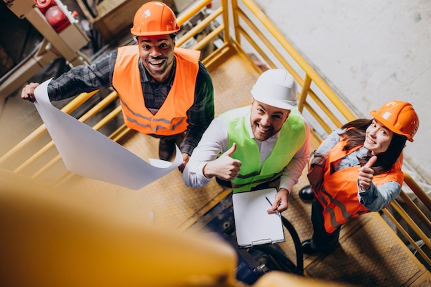 Drie fabrieksarbeiders met veiligheidshoeden bespreken fabricageplan