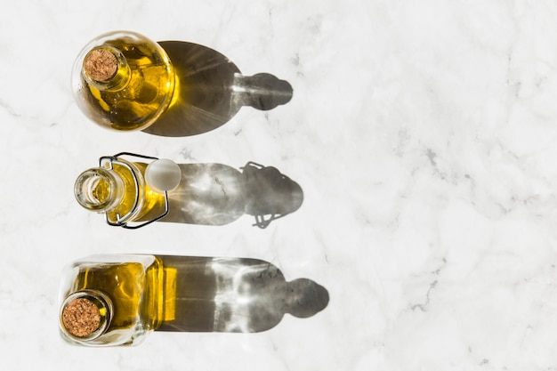 Drie flessen maagdelijke gezonde olijfolie met schaduw op vloer