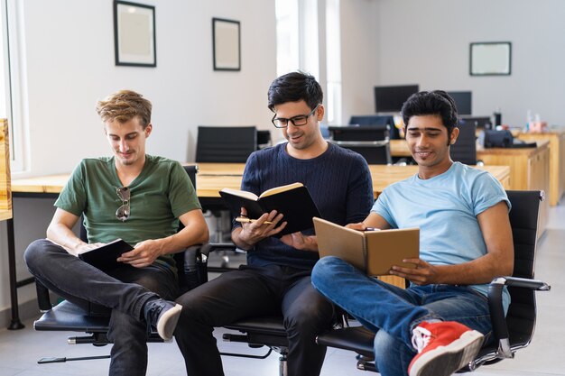 Drie glimlachende medestudenten die studieboeken bestuderen lezen