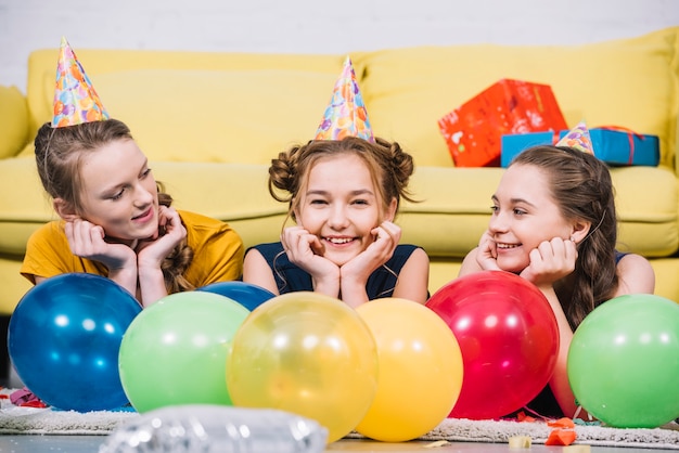 Drie glimlachende meisjes die op tapijt met kleurrijke ballons thuis liggen