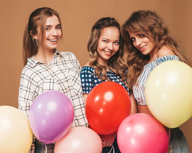 Drie glimlachende mooie vrouwen in de kleren van de geruite overhemdszomer. Meisjes poseren. Modellen met kleurrijke ballonnen. Plezier, klaar voor de verjaardag van het feest