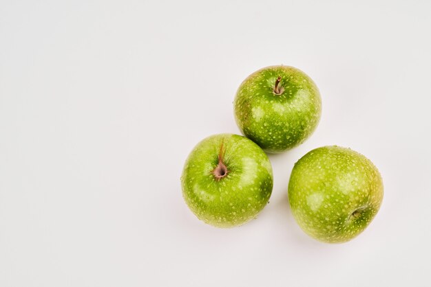 Drie groene appels op wit oppervlak.