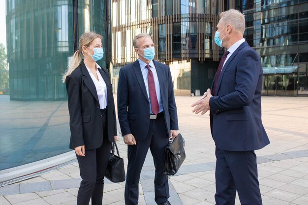 Drie inhoudspartners in maskers bespreken deal buiten. Zelfverzekerde succesvolle managers die op straat staan en werken tijdens de coronaviruspandemie. Onderhandeling en partnerschap concept