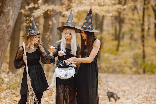 Drie jonge meisjesheksen in bos op Halloween. Meisjes dragen zwarte jurken en kegelhoed. Heks die een tovenaarmateriaal houdt.