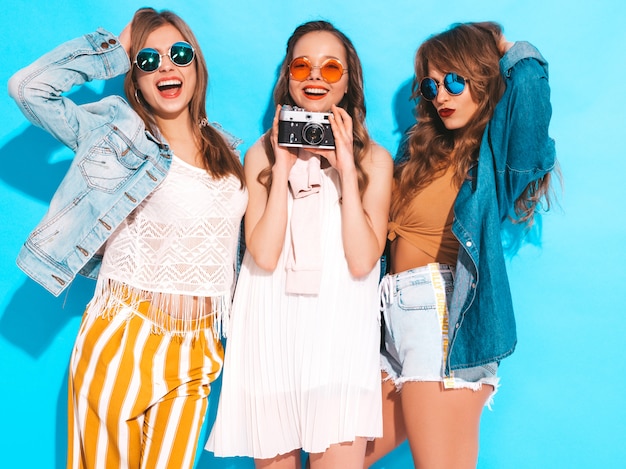 Drie jonge mooie glimlachende meisjes in trendy zomer casual jurken en in zonnebril. Sexy zorgeloze vrouwen poseren. Foto's maken met een retro camera