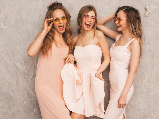 Drie jonge mooie glimlachende meisjes in trendy zomer lichtroze jurken. Sexy zorgeloze vrouwen poseren. Positieve modellen in ronde zonnebril met plezier