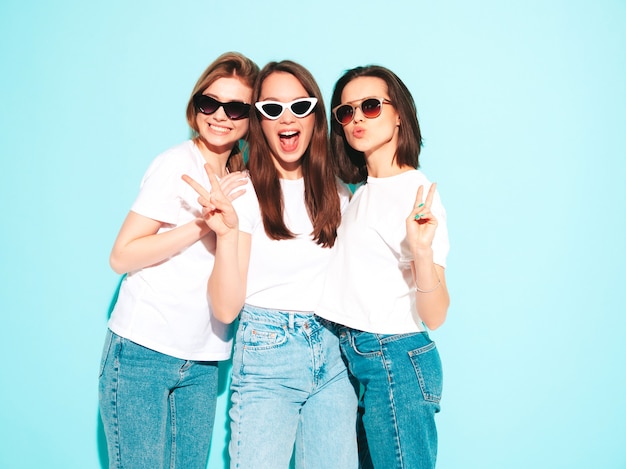 Drie jonge mooie lachende hipster-vrouwen in trendy dezelfde zomer witte t-shirt en jeans kleding