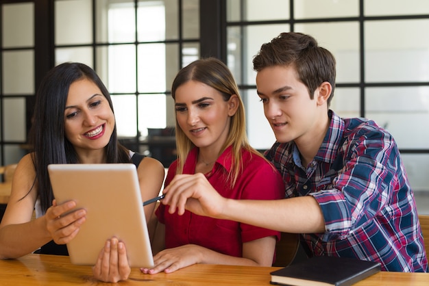 Drie jonge positieve studenten die digitale tablet in koffie gebruiken