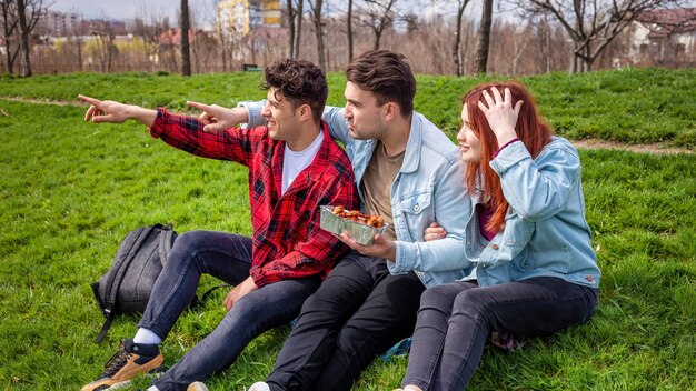 Drie jonge vrienden die op het gras zitten en voedsel in een park houden