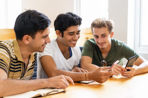 Drie lachende studenten studeren, met behulp van smartphones