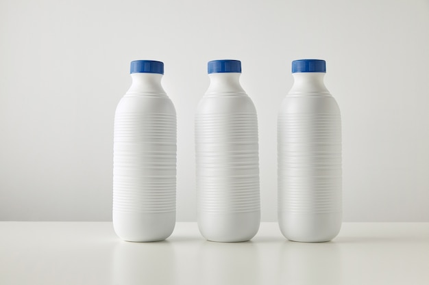 Gratis foto drie lege witte plastic flessen met blauwe doppen in rij geïsoleerd op tafel in het midden