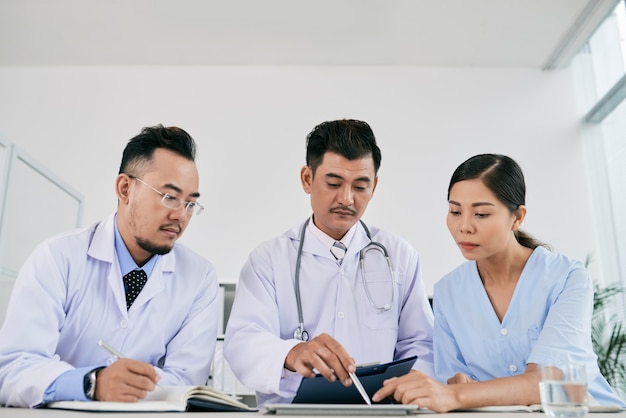 Drie mannelijke en vrouwelijke medische professionals die de medische geschiedenis van de patiënt bespreken