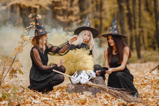 Drie meisjesheksen in bos op Halloween. Meisjes met zwarte jurken en kegelhoeden. Heksen maken een toverdrank.