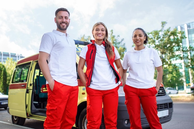 Drie multiraciale paramedici staan voor ambulancevoertuig met draagbare apparatuur