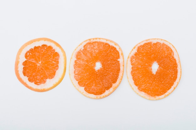 Drie plakken van sinaasappel die in rij op witte achtergrond worden geschikt