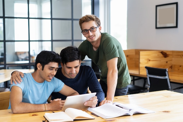 Drie positieve studenten die op tabletcomputer samen doorbladeren