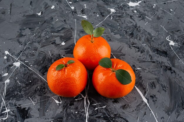 Drie sappige mandarijnvruchten met bladeren op marmeren oppervlak.