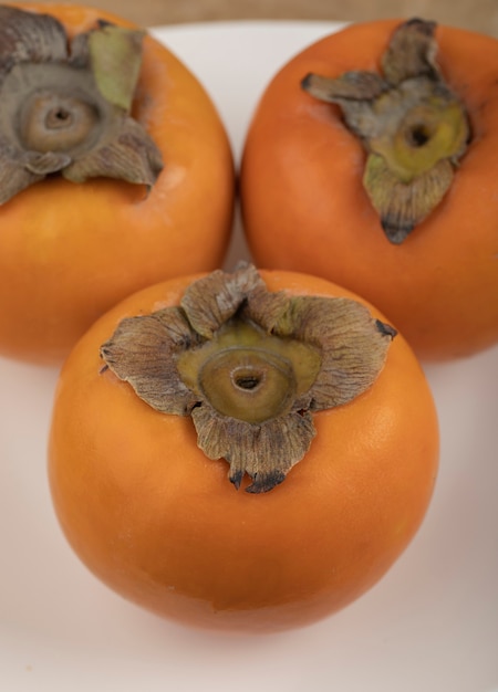 Drie smakelijke fuyu-persimmon op witte plaat op marmeren oppervlak