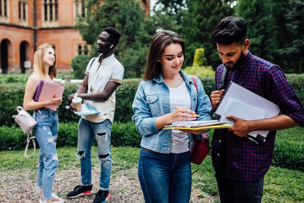 Drie studenten praten met elkaar buiten op de binnenplaats van een universiteit.