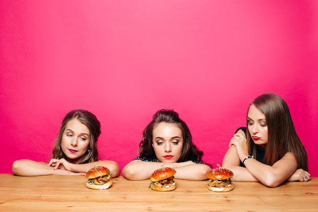 Gratis foto drie trieste meisjes op dieet kijken naar hamburgers op tafel